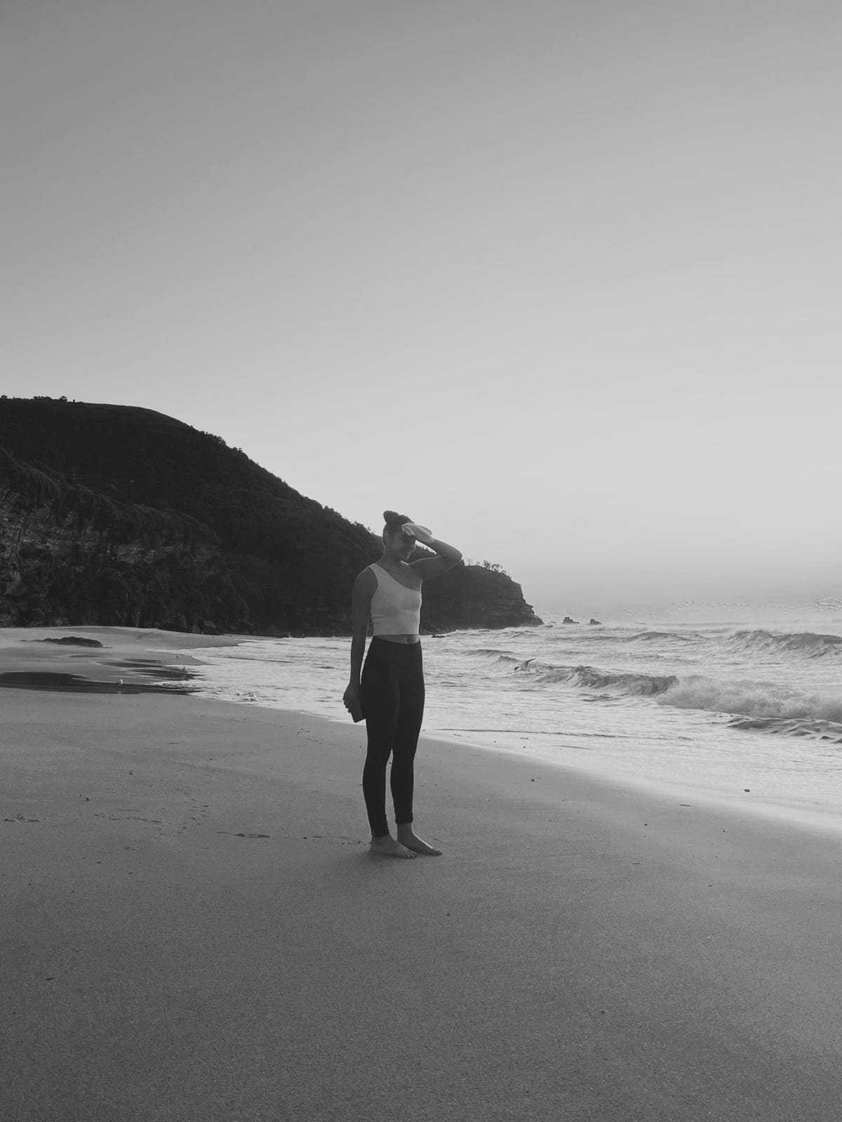 A woman stretching by the sea, in black and white