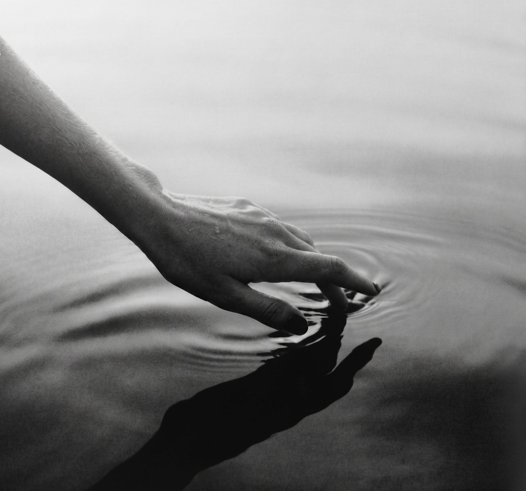 A hand touching the surface of still water, in black and white
