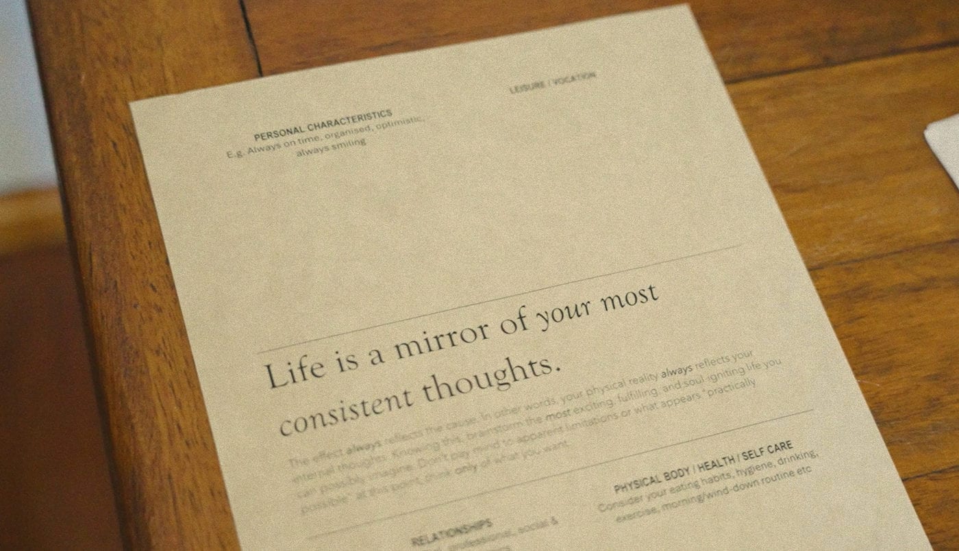 A printed card on a wooden table reading “Life is a mirror of your most consistent thoughts”