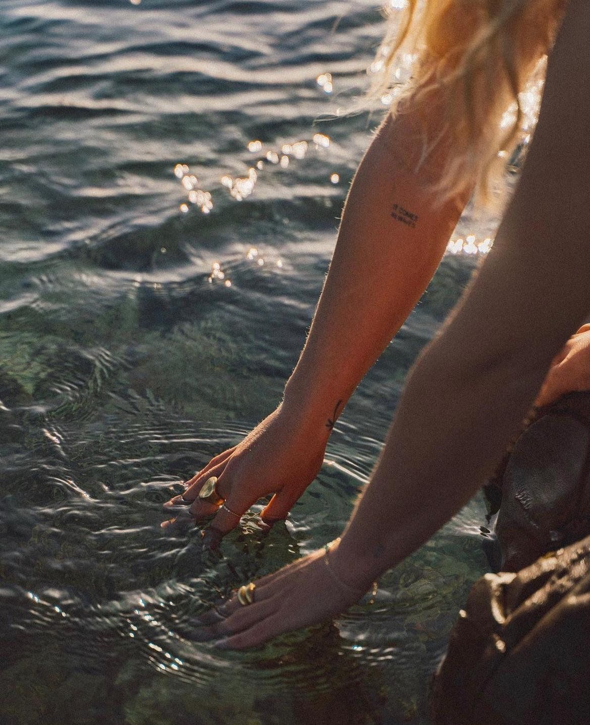 Hands reaching into gently moving water at golden hour